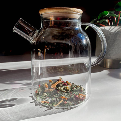 Clear glass teapot with wooden lid and handle on a white surface