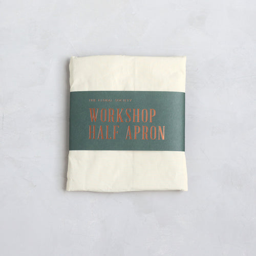 Folded workshop half apron with a label on a light gray background