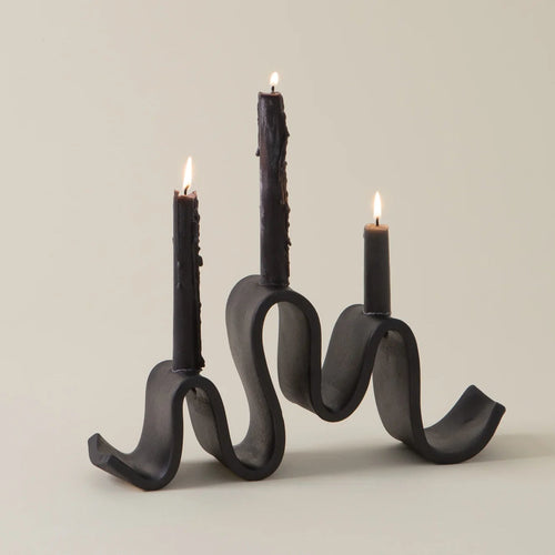 Black wavy candle holder with three lit candles on a beige background