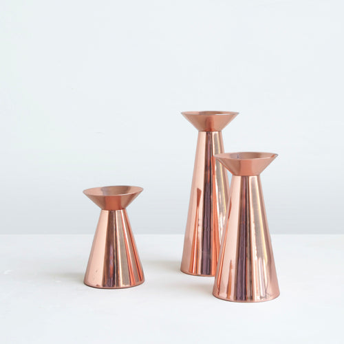 Our copper grand taper holders offer a modern take on a classic object, instantly elevating any setting. The luminous copper finish reflects light and lends a sense of movement to a table or mantlepiece, especially when paired or gathered as a trio. Each copper plated holder is sized to fit a standard taper candle.